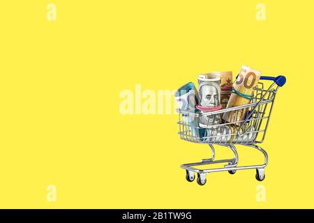 Shopping cart full of money isolated on Yellow background. Multi currency basket concept. online shopping or financial success Stock Photo