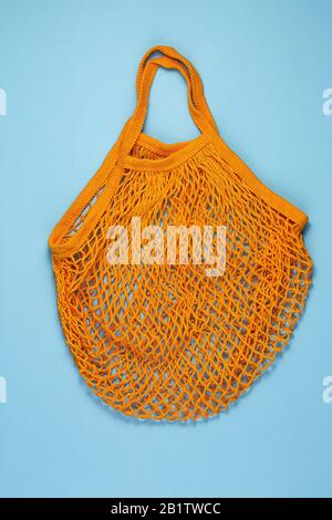 Orange cotton mesh bag on blue paper background.Reusable shopping bag on color background. Ecological, Zero waste concept. Top view, flat lay, copy sp Stock Photo