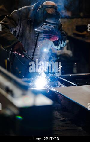 worker in protective uniform and mask welding metal. man using electric welding machine Stock Photo