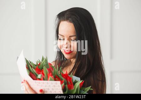 Beautiful caucasian brunette woman holding fresh blossoming red tulips flower bouquet. Stock Photo