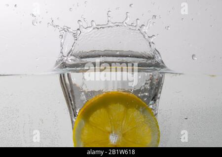 a slice of lemon falls into the water from above and creates water splashes Stock Photo