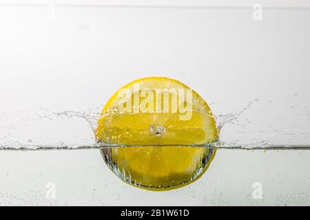 a slice of lemon falls into the water from above and creates water splashes Stock Photo