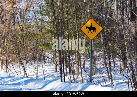 A yellow diamond sign has a pictogram of a person riding a horse, indicating a horseback riding crossing on a rural road. In the countryside during wi Stock Photo