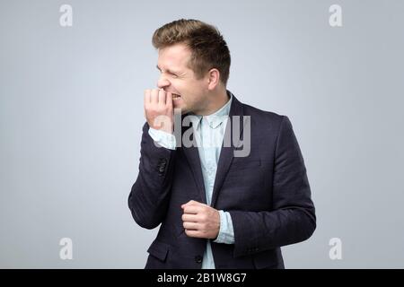 Caucasian young man in suit biting nails feeling nervous. Bad habbit concept. Stock Photo