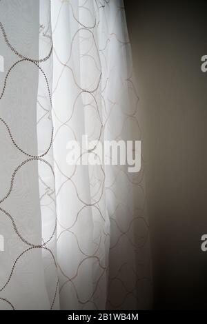 Light comes through sheer curtains with stitched pattern seen from the side inside, as a breeze makes them sway. Soft and blurry. Colour photo. Stock Photo