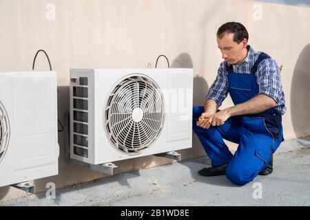 Young Male Technician Repairing Air Conditioning System On Roof Stock Photo
