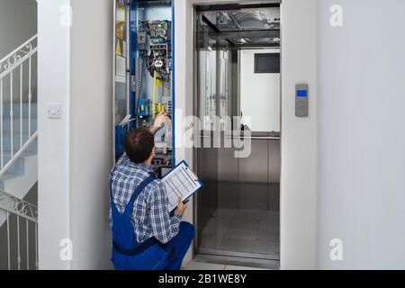 Technician Repairing Control Panel Of Broken Elevator Stock Photo