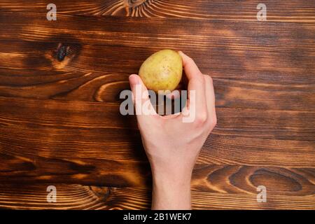 A hand holds a potato on a wooden burnt background. Top view. Close up. Stock Photo