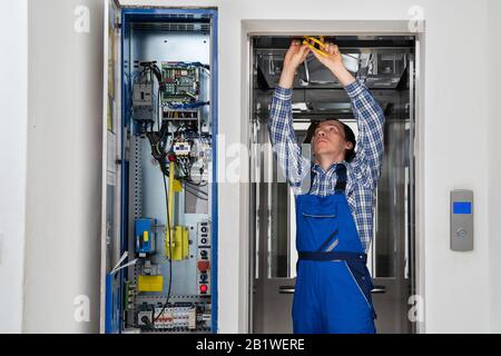 Technician Repairing Control Panel Of Broken Elevator Stock Photo