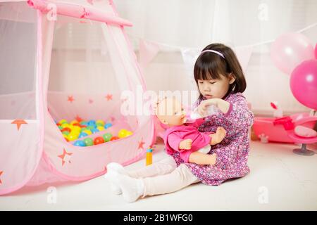 toddler girl pretend play baby care at home against white background Stock Photo