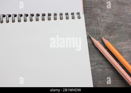 Open sketchbook on a spiral with white pages and a pencil on a rough dark textured wooden table. Top view, copy space Stock Photo