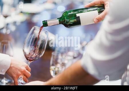 Waiter pouring red wine from a green bottle into a glass Stock Photo