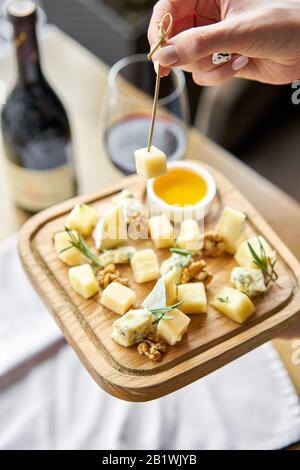 Girl holding piece of parmesan cheese on a skewer and wooden plate with cheese. Delicious cheese mix with walnuts, honey. Food for wine. Stock Photo