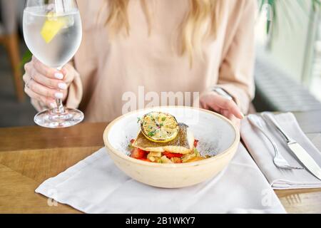 Roasted Halibut with vegetables, paprika pepper and pumpkin cream. Lunch in a restaurant, a woman eats delicious and healthy food. Dish decorated with Stock Photo