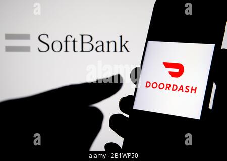 Doordash company logo on a smartphone hold in hand with SoftBank logo on the blurred laptop screen behind. Concept. Not a montage, real photo. Stock Photo