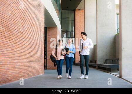Asian three students are walking and talking together in university hall during break in University. Education, Learning, Student, Campus, University, Stock Photo