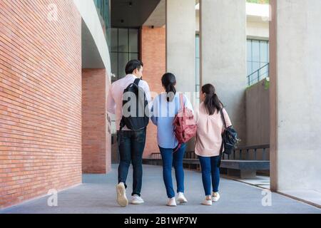 Asian three students are walking and talking together in university hall during break in University. Education, Learning, Student, Campus, University, Stock Photo