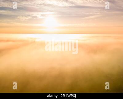 Foggy sunrise - flight above very thick clouds foggy sunrise over forest landscape in Sweden - golden sun light. Copy space Stock Photo