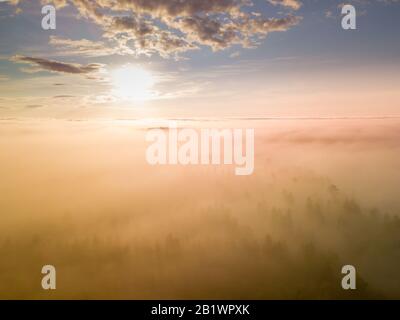 drone photo above very thick clouds foggy sunrise over forest landscape and village in North Sweden - golden sun light Stock Photo