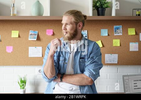 Millennial man freelancer looking away dreaming standing at home office Stock Photo