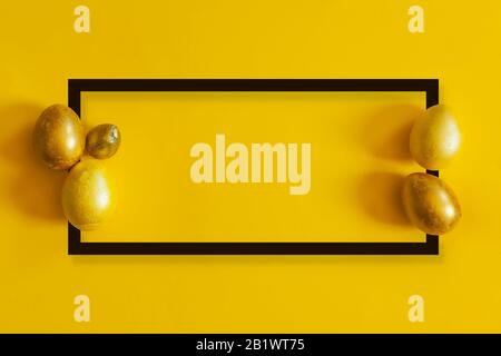 Golden colored easter eggs on the yellow background. View from above. Black border frame. Top view. Flat lay image of easter festive holiday Stock Photo