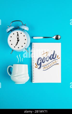 Coffee mug with notebook and clock with quote Good Morning Stock Photo