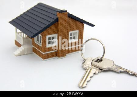 A small house and some keys on a white table symbolizing the purchase or mortgage of a house Stock Photo