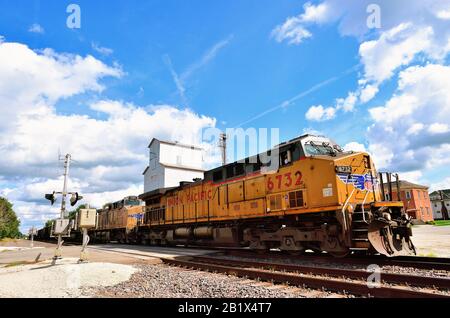 Creston, Illinois, USA. A Union Pacific empty coal train, lead by three locomotive units passing a grain elevator and grade crossing. Stock Photo