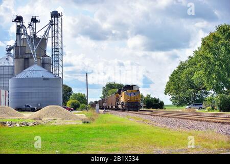 Malta, Illinois, USA. A helper locomotive unit assists a Union Pacific coal train, lead by three locomotive units, as it passes a farming cooperative. Stock Photo