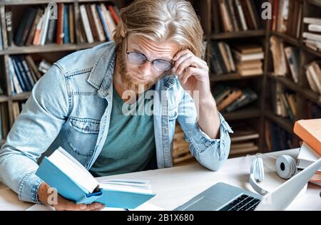 Young focused man library desk surprised look at open book volume copy space. Stock Photo