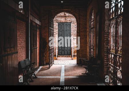 GONZALEZ CATAN, ARGENTINA, SEPTEMBER 28, 2019: Passage leading to an old brick arch with rusty open iron gate, heading to a broken blind. Stock Photo