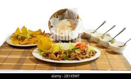Plate of beef fajitas with pepper and onion strips accompanied by tomato and lettuce with a basket with corn tortillas on white background Stock Photo