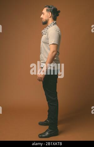 Studio shot of young bearded Indian man wearing stylish clothes against brown background Stock Photo