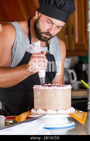 male baker decorating a chocolate birthday cake with strawberry moose frosting Stock Photo