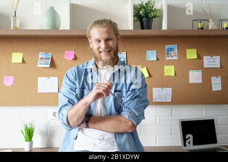 Smiling confident millennial man look at camera stand at workspace Stock Photo