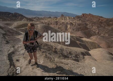 A solo female hiker walks a trail through the hills and desert in Death Valley National park in California. Stock Photo
