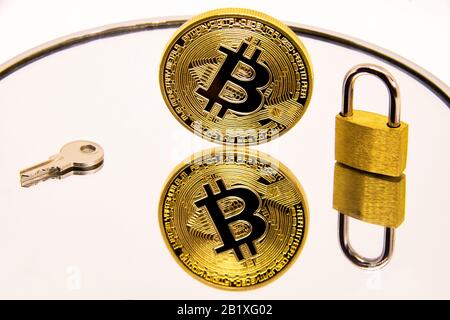 Gold bitcoin coin on a white mirror surface with a golden padlock and key. cryptocurrency Conceptual image of a cryptocurrency golden bitcoin coin on Stock Photo