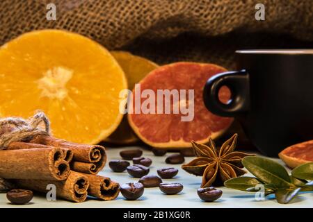 A black mug of coffee next to cinnamon with puddings and sliced oranges with green coffe leaws Stock Photo