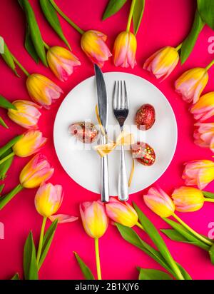 Beautiful luxury easter table cutlery settings as knife, fork with colorful tulips and gold painted eggs with glitters on red surface. Holiday backgro Stock Photo