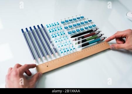 A Person's Hand Arranging Pencils And Multi Colored Pushpins In A Row On White Background Stock Photo