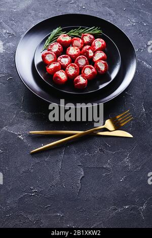 Party food ricotta stuffed hot cherry peppers served on a black plate with rosemary sprigs and golden cutlery on a dark concrete background, vertical Stock Photo