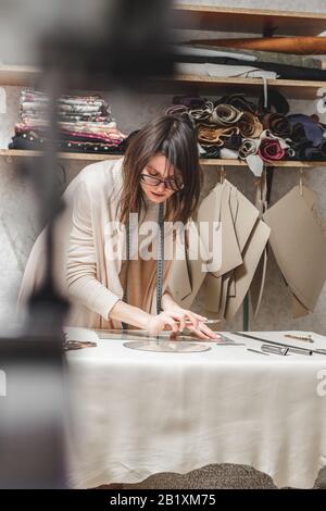 Leather craftswoman working making measurements in patterns at table in workshop studio. Small business and mastership concept Stock Photo