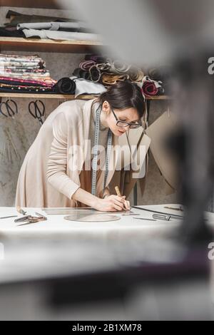 Leather craftswoman working making measurements in patterns at table in workshop studio. Small business and mastership concept Stock Photo