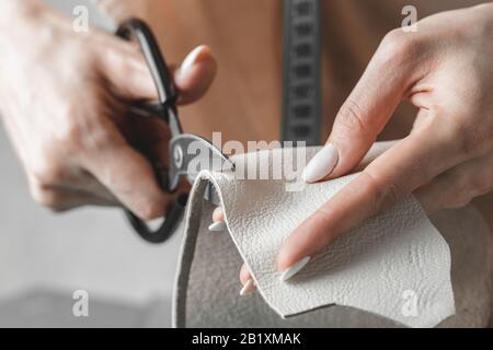 Female handbag designer measuring leather and cutting out details in a workshop studio Stock Photo