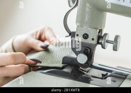 Young white woman stitching leather using a sewing machine Stock Photo