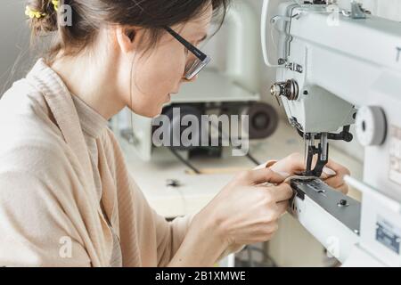 Young white woman stitching leather using a sewing machine Stock Photo
