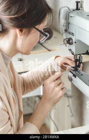 Young white woman stitching leather using a sewing machine Stock Photo