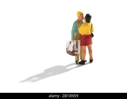 Small miniature couple, man and woman in casual clothes, standing and kissing. The man holding a bag or a suitcase in his hand. Isolated on white back Stock Photo