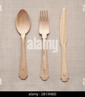 Unpainted wooden cutlery - spoon, fork and knife sitting on rustic tablecloth viewed from above Stock Photo