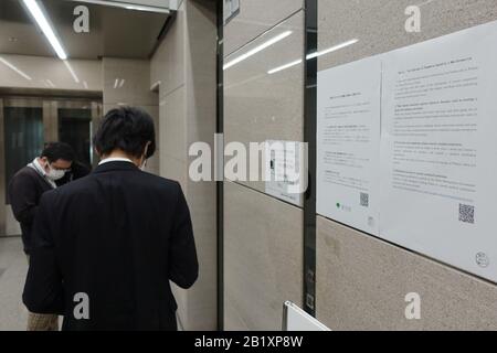 Tokyo, Japan. 27th Feb, 2020. People wait for an elevator beside a notice of coronavirus in an office building in Tokyo, Japan, Feb. 27, 2020. Japan's Education Minister Koichi Hagiuda on Friday requested all students to remain indoors and not to attend schools that have been closed to contain COVID-19. Credit: Du Xiaoyi/Xinhua/Alamy Live News Stock Photo